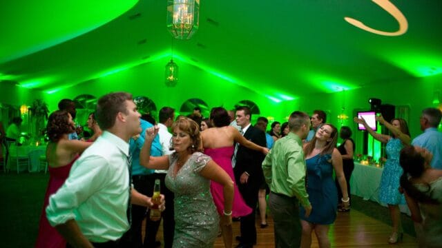 People dancing in a green-lit room at a reception, with some dressed in formal attire.